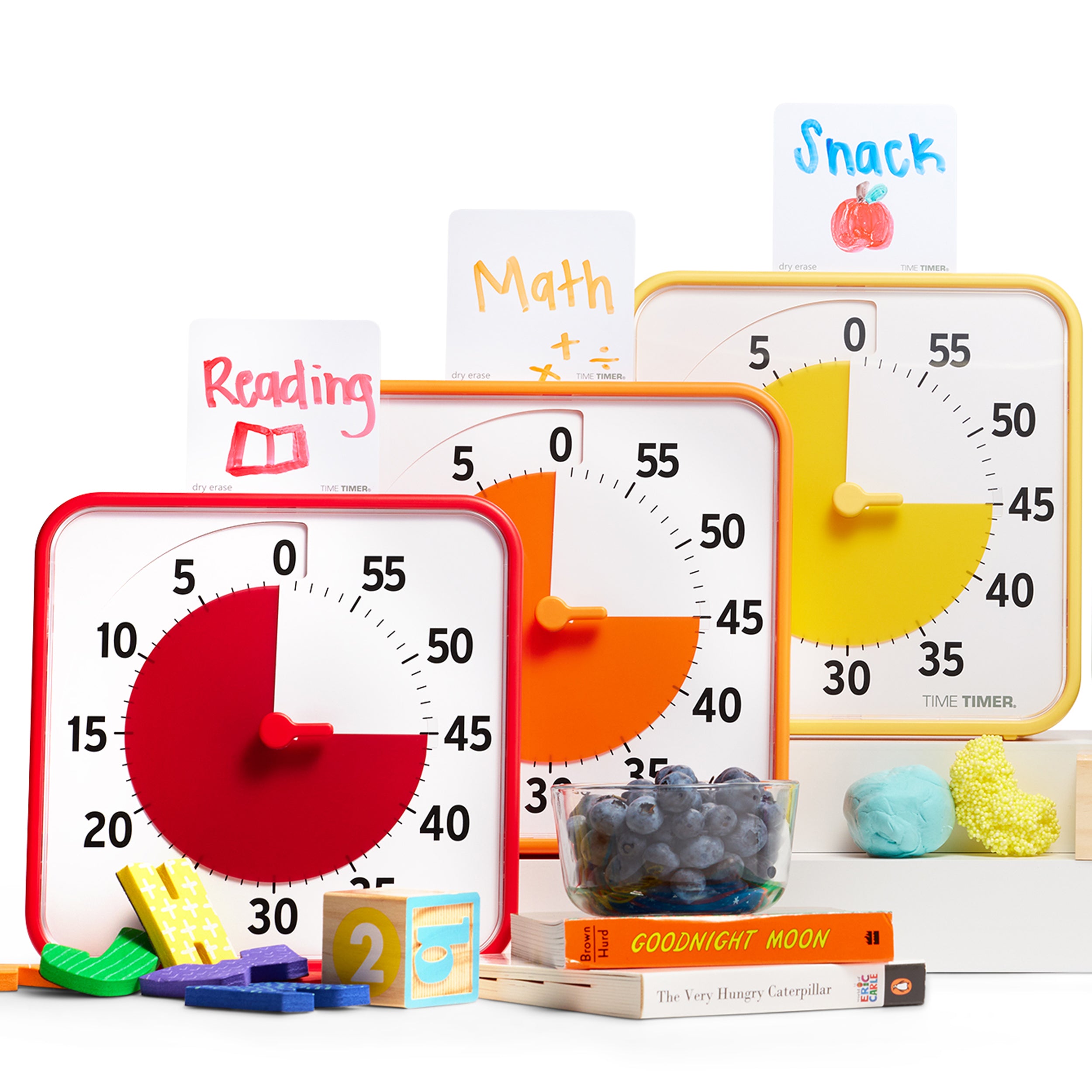 The Time Timer Original Learning Center Classroom Set timers are shown with one Dry Erase Activity Card on top of each. The red timer has a card that states "Reading" on it. The Orange timer has a card that states "Math." And the Yellow timer displays a card that reads "Snack" with a drawing of an apple. 