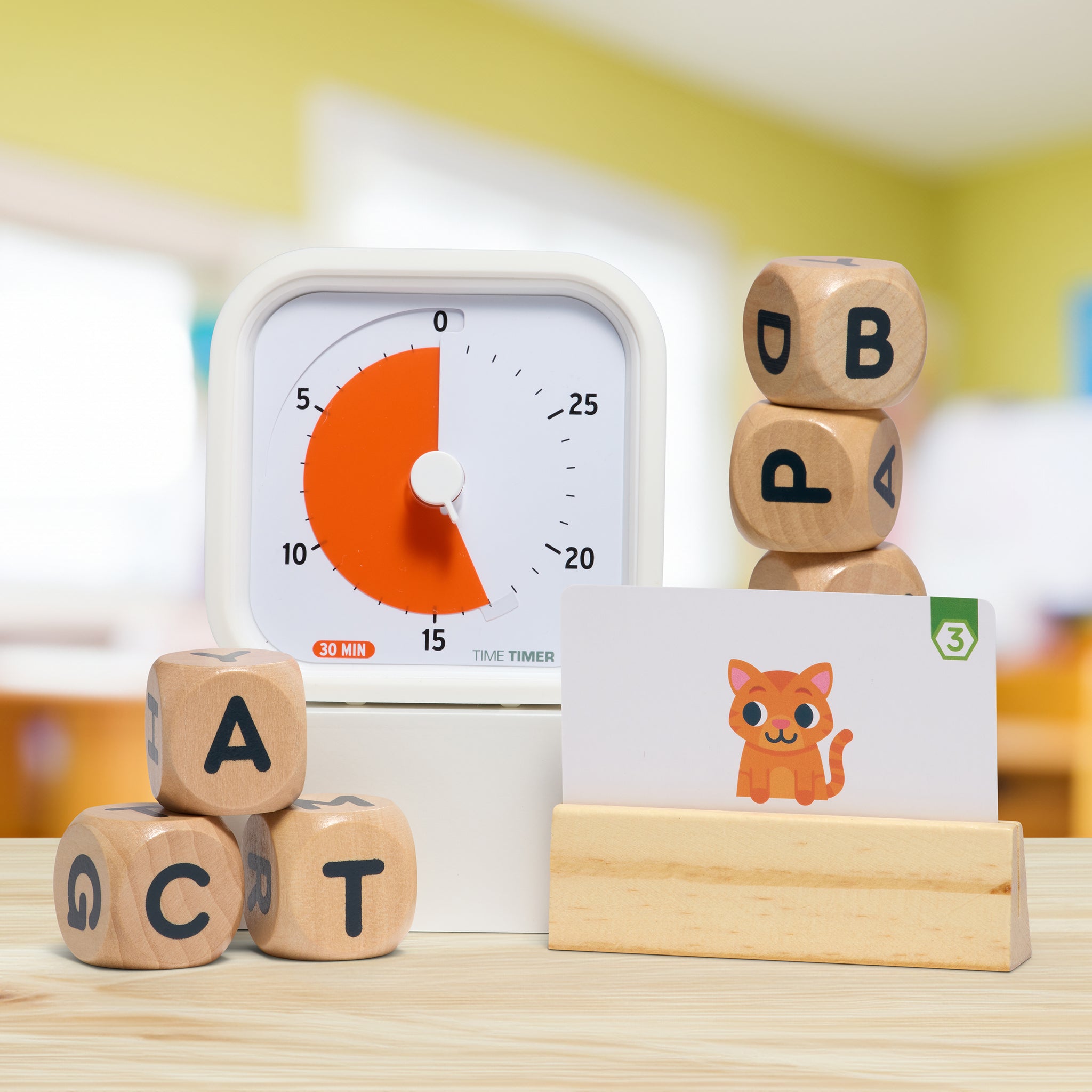 The Time Timer MOD Education Edition 30 minute timer is shown in a classroom setting alongside some blocks with letters on them and a picture card showing an orange cat.