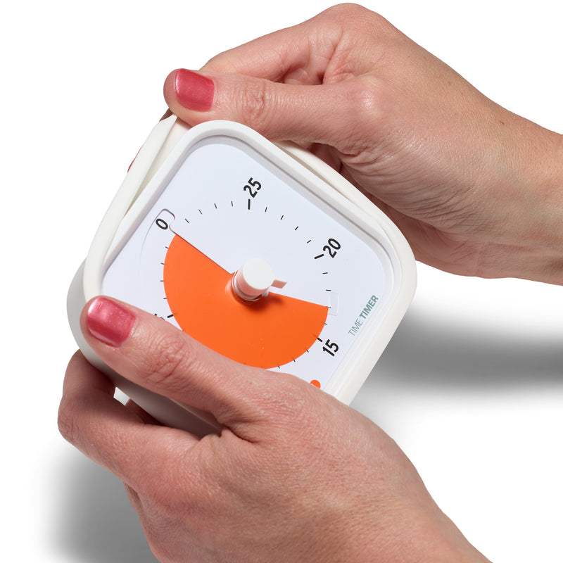 The Time Timer MOD Education Edition 30 minute visual timer is shown, held by two hands. One hand is peeling off the soft silicone case of the timer.
